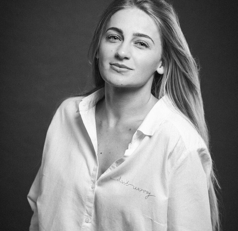 A greyscale shot of an attractive caucasian blonde female in a white shirt posing on a brown background