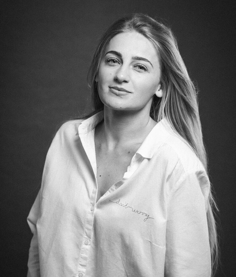 A greyscale shot of an attractive caucasian blonde female in a white shirt posing on a brown background
