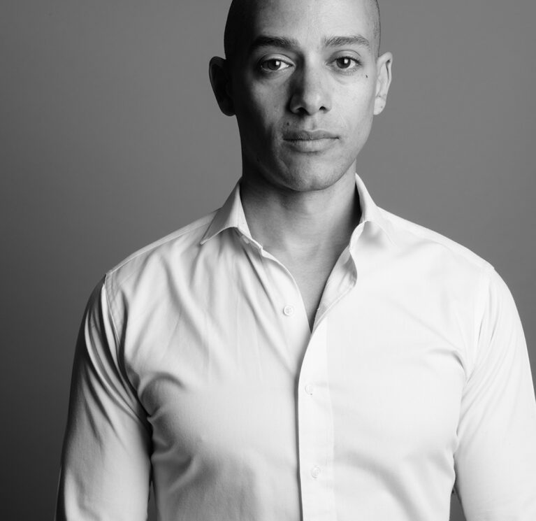 Studio shot of handsome bald businessman wearing white shirt against gray background in black and white